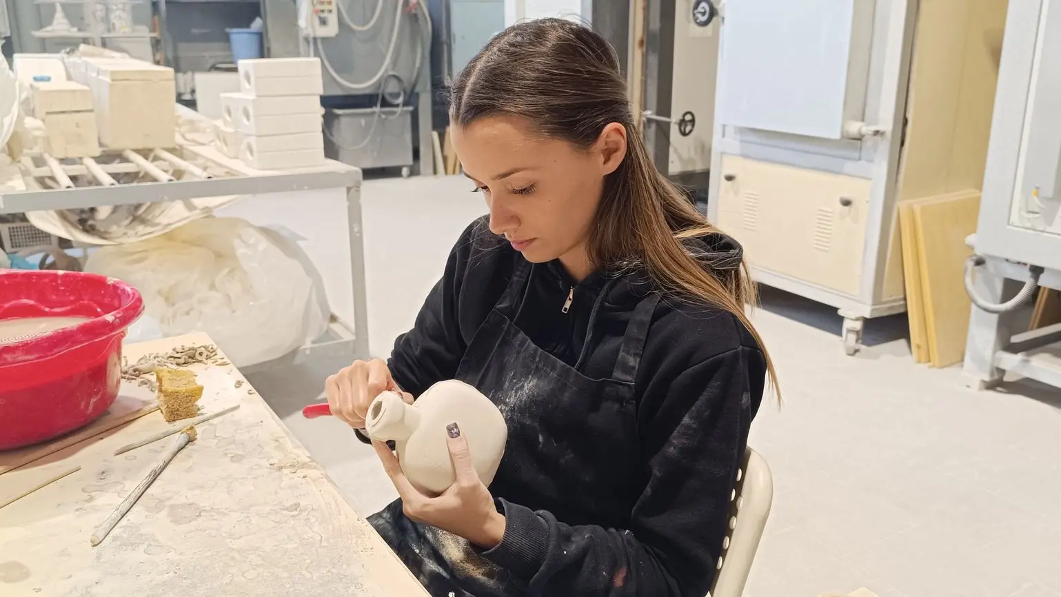 donna che seduta dipinge un lavoro in ceramica